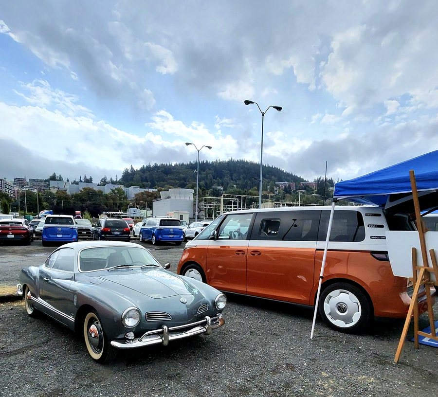 A grey vintage Volkswagen Karmann Ghia parked beside an orange and white ID. Buzz.