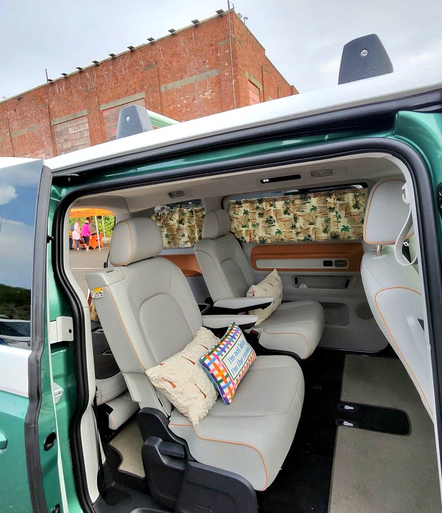 Second-row captain's chairs in cream leather inside a green ID. Buzz, with palm-print curtains drawn across the side windows.