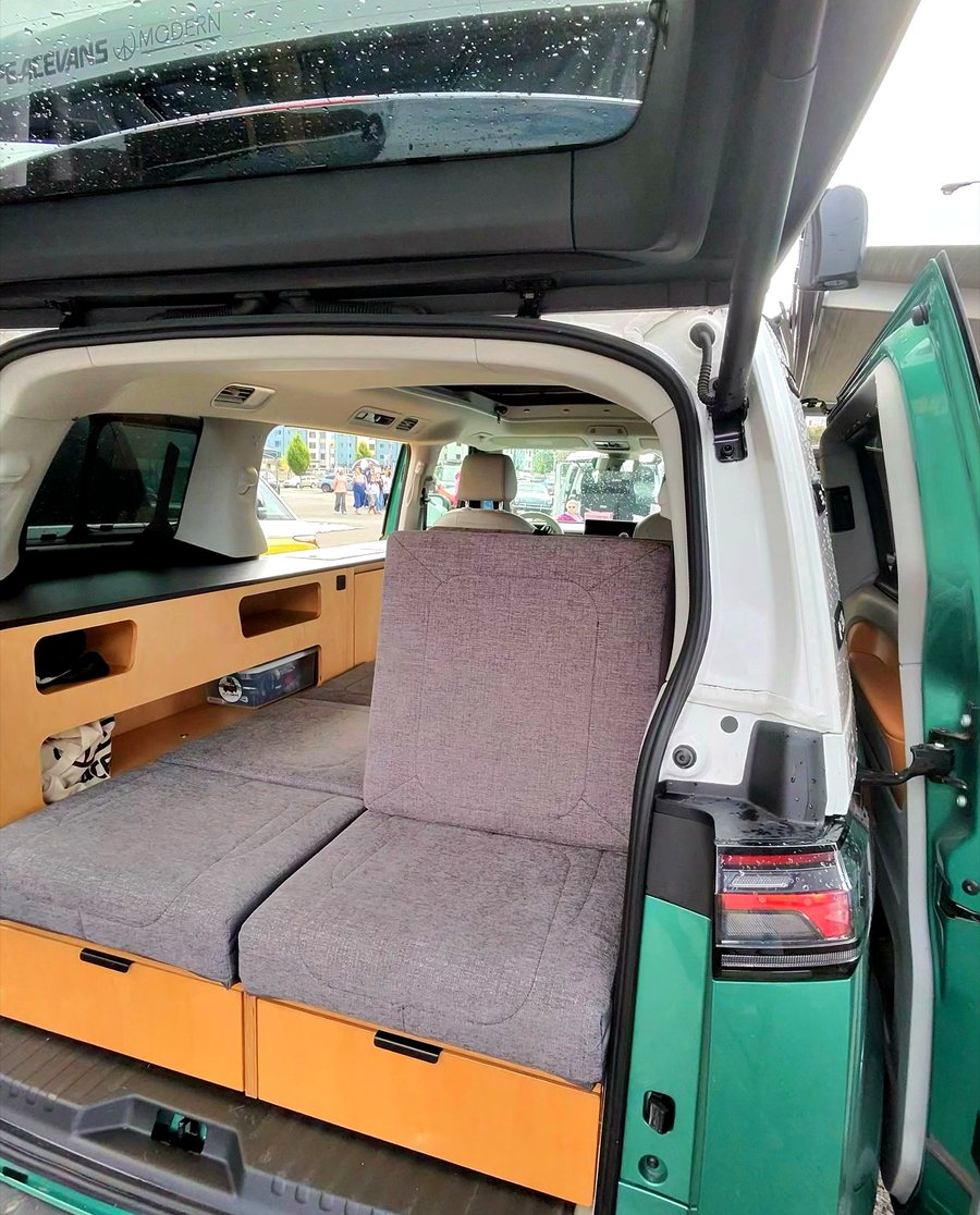 Rear view into a green ID. Buzz with bed cushions folded into a bench and birch storage cabinets along the side wall.