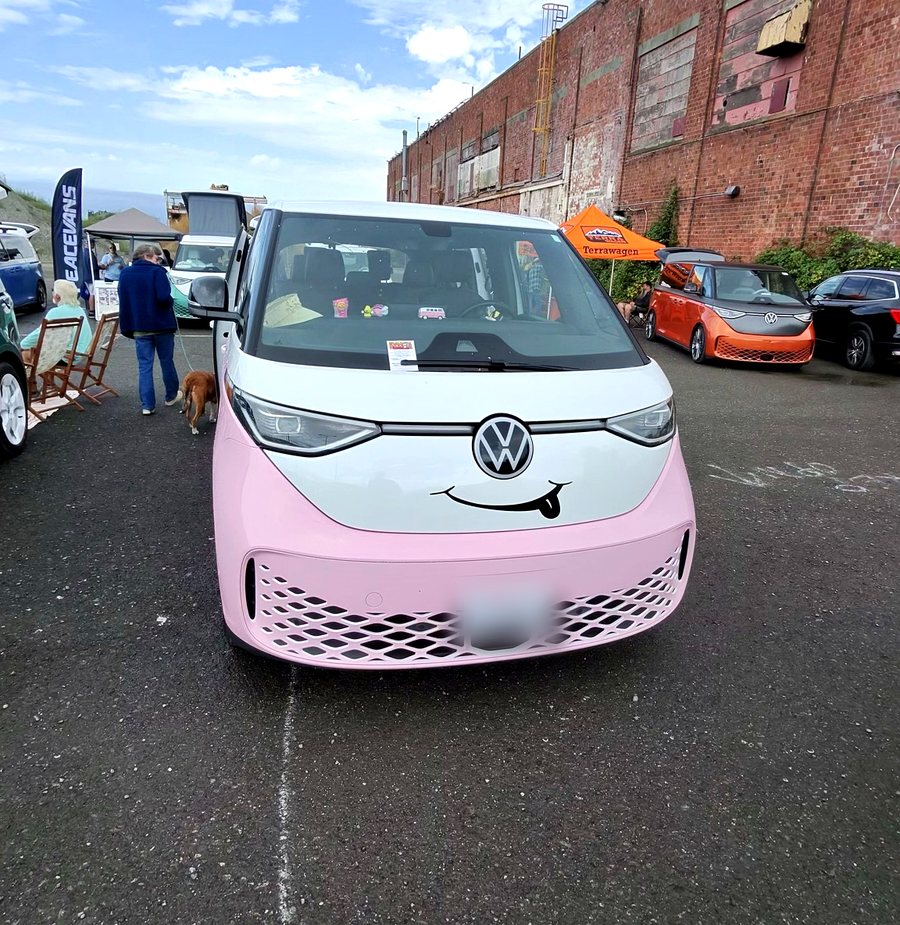 A pink and white wrapped ID. Buzz photographed head-on with a smiling face decal applied below the VW badge.