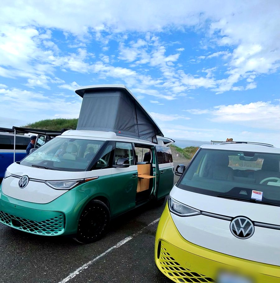 A green and white ID. Buzz with an aftermarket pop-top roof raised, parked next to a yellow ID. Buzz.