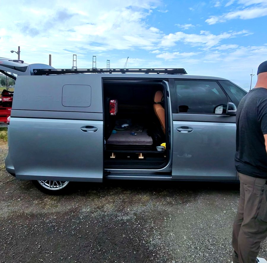 Side view of the same silver ID. Buzz Cargo with its sliding door open, revealing a raised sleeping platform with a mattress and bedding inside.