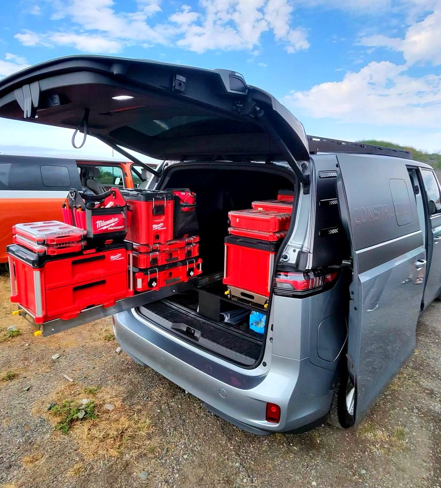 The rear hatch of a silver ID. Buzz Cargo open, loaded with stacked red Milwaukee Packout tool cases, with louvered vents cut into the blanked side panel.